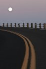Lua cheia sobre estrada curva com linhas amarelas no crepúsculo — Fotografia de Stock