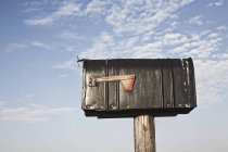 Поштова скринька на дерев'яному стовпі проти хмарного неба — стокове фото