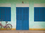 Bicicleta estacionada no alpendre da frente com porta de madeira azul e janelas — Fotografia de Stock