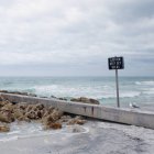Segnale di avvertimento sulla spiaggia rocciosa con gabbiano seduto sul muro — Foto stock