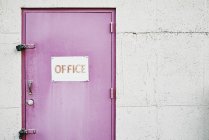 Office sign on locked door in pink on grey wall — Stock Photo