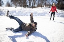Young man falling while ice skating on frozen lake in winter — Stock Photo