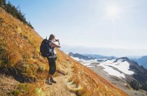 Mujer tomando fotos de montañas remotas en la ladera del Monte Baker, Washington, EE.UU. - foto de stock