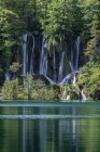 Cachoeira derramando sobre formações rochosas para lago remoto — Fotografia de Stock