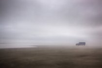 Caminhão estacionado na areia molhada na praia nebulosa em tempo tempestuoso — Fotografia de Stock