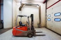 Forklift machinery parked in warehouse garage with metal door — Stock Photo
