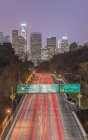Ciudad de Los Ángeles skyline sobre carretera ocupada iluminado por la noche, California, Estados Unidos - foto de stock