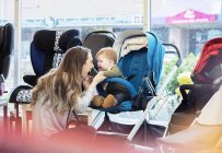 Caucasian mother and baby son testing strollers while shopping in stroller store — стокове фото