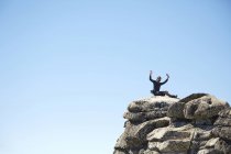 Hiker cheering on rocky hilltop under blue sky — Stock Photo