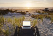 Ordinateur portable sur chaise longue donnant sur le coucher du soleil sur la plage — Photo de stock