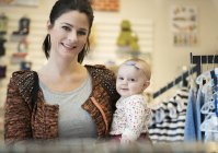 Caucasian mother and baby daughter shopping in clothing store — стокове фото