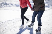 Bassa sezione di coppia pattinaggio su ghiaccio sul lago ghiacciato innevato in inverno — Foto stock