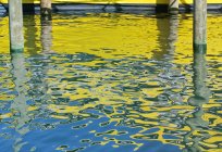 Barco amarelo refletindo na água com postes de madeira . — Fotografia de Stock