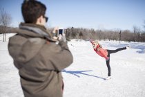 Joven hombre tomando foto de la mujer patinaje sobre hielo en el lago congelado en invierno - foto de stock