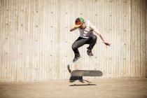 Кавказька людина робить Скейт трюк біля дерев'яної стіни — стокове фото