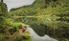 Hiker crouching at still lake in remote mountains, Azore Islands, Portugal — Stock Photo
