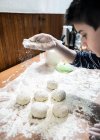 Caucasian boy sprinkling flour over dough balls — стокове фото