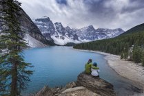 Vista trasera de la pareja sentada en rocas admirando el paisaje del lago de montaña, Parque Nacional Banff, Canadá - foto de stock