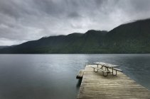 Picnic table on wooden pier at still remote lake — Stock Photo
