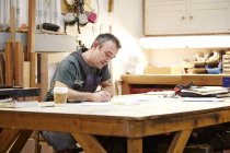 Carpenter sketching at table in workshop interior — Stock Photo