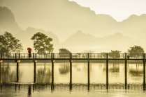 Mountains and teen monk under umbrella on bridge reflecting in still lake, Hpa-an, Kayin, Myanmar — Stock Photo