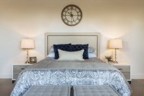 Кровать в спальне с винтажными часами на стене — стоковое фото