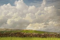 Mur de pierre et champ herbeux sous les nuages dans le paysage rural — Photo de stock