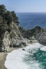 Cascata che si riversa nelle onde che si riversano sulla spiaggia rocciosa, Julia Pfeiffer Burns State Park, California, USA — Foto stock