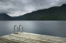 Ladder on wooden pier at still remote lake — Stock Photo