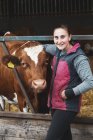 Jovem mulher de pé ao lado de vaca Guernsey em uma fazenda . — Fotografia de Stock