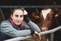 Portrait of young woman standing next to Guernsey cow on farm. — Stock Photo