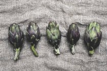 Vista en ángulo alto de alcachofas frescas sobre un paño gris - foto de stock