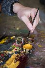 Close-up of female hand dipping paintbrush into small pot of yellow oil paint. — Stock Photo