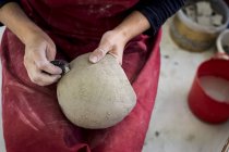 Мидсекция керамического художника в красном фартуке сидит в мастерской, работает над глиняной вазой . — стоковое фото