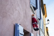 Figura di Babbo Natale appesa alla corda dalla finestra di casa con facciata rosa . — Foto stock