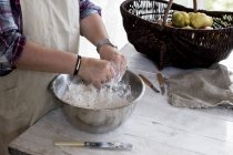 Close up of person wearing apron standing in kitchen, mixing ingredients for a crumble in metal bowl. — Stock Photo
