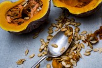 Close-up of silver tablespoon and purple pumpkin with orange flesh cut in half. — Stock Photo