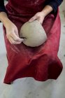 Крупный план керамического художника в красном фартуке, сидящего в мастерской и работающего над глиняной вазой . — стоковое фото