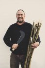 Homme barbu tenant bec crochet et tas de piquets en bois pour la pose de haies traditionnelles, souriant à la caméra . — Photo de stock