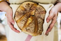 Gros plan des mains de la personne tenant une miche ronde de pain fraîchement cuite . — Photo de stock