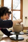 Donna seduta in laboratorio di ceramica e che lavora su vaso di argilla . — Foto stock