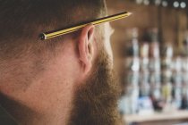 Nahaufnahme eines Bleistifts über dem Ohr eines bärtigen Mannes mit braunen Haaren. — Stockfoto