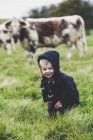 Petit garçon debout sur le pâturage avec des vaches anglaises Longhorn en arrière-plan . — Photo de stock