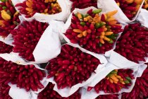 High angle close-up of large bunches of fresh red and orange chilies at Italian market stall. — Stock Photo