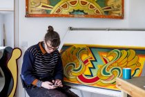 Artista donna seduta disegnando in corso al tavolo da disegno in officina e controllando il cellulare . — Foto stock