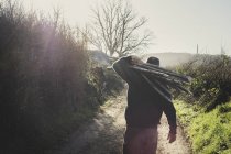 Vue arrière de l'homme marchant sur le chemin rural, portant un tas de pleureurs en bois utilisés dans la construction traditionnelle de haies . — Photo de stock