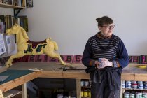 Frau sitzt in Werkstatt neben traditionellem Holzkarussell Galopperpferd aus Karussell. — Stockfoto