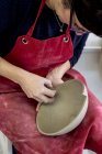 Frau in roter Schürze sitzt in Keramikwerkstatt und arbeitet an Tonschale. — Stockfoto