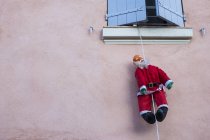 Weihnachtsmann-Figur hängt an Seil aus Fenster des Hauses mit rosa Fassade. — Stockfoto
