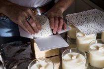 Close up of person wrapping handmade white jar candles. — Stock Photo